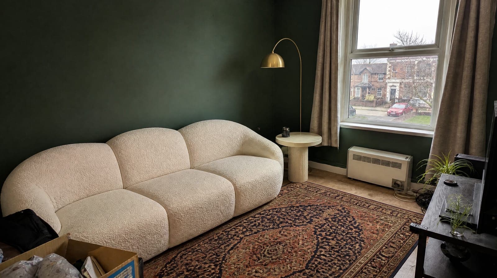 The same room with forest green walls, a cream curved sofa, a Persian rug and a brass lamp